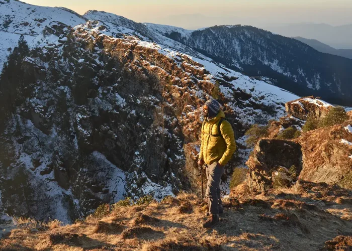 A trekker takes a break to gaze at the snow studded peaks on Brahmatal Trek.