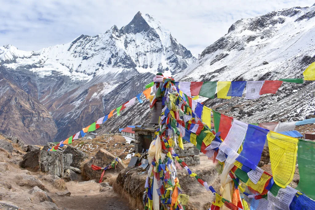 Colorful prayer flags flutter in the wind in front of a snow-capped mountain, in the Annapurna Sanctuary range.