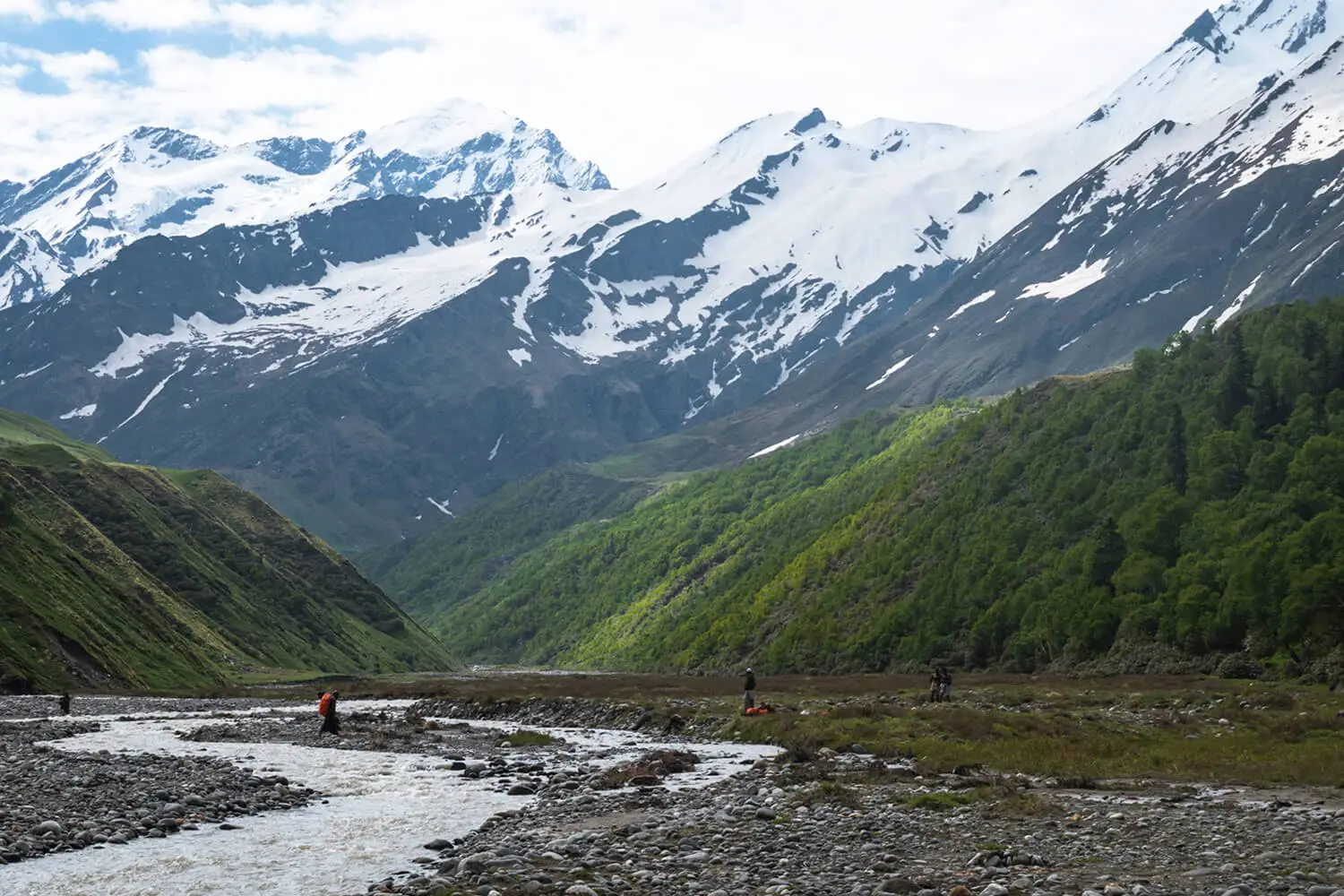 A trekker enjoying icy cold water of mountain river with snow studded peaks in the background on Bali Pass Trek in autumn