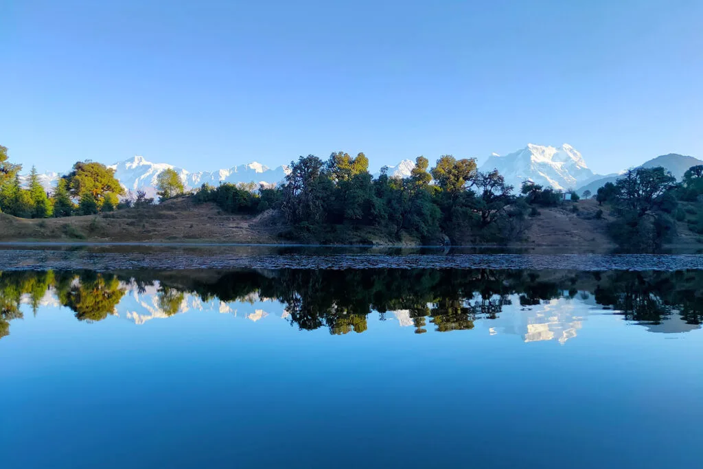 A crystal-clear lake at Deoriatal Rohini Bugyal reflecting a vibrant blue sky