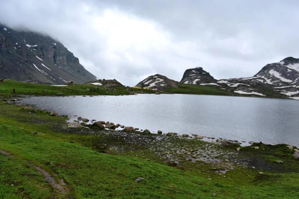 A peaceful scene of the Tarsar Marsar lake with crystal-clear water reflecting snow-capped mountains.